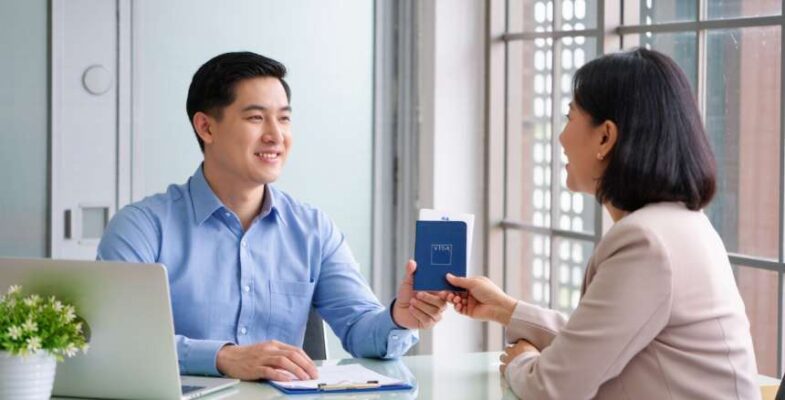 Dịch Vụ Gia Hạn Visa Mỹ Tại Hà Nội 2026 - Uy Tín, Minh Bạch Chi Phí 5 Dịch vụ gia hạn visa Mỹ trọn gói tại Hà Nội, chuyên viên đang trao hộ chiếu cho khách hàng.