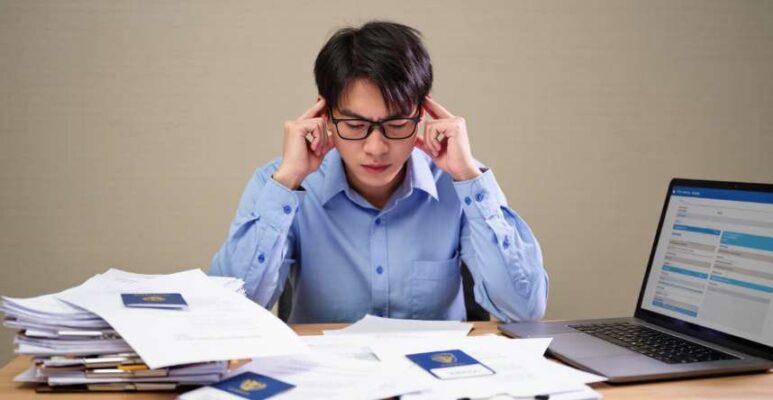 Một người căng thẳng và mệt mỏi bên chồng giấy tờ phức tạp khi tự làm hồ sơ xin visa Trung Quốc.